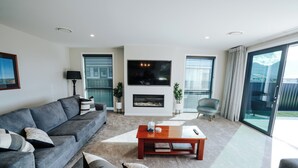 A living room with a sofa, a coffee table, a flat-screen TV, and a fireplace. - Fiordland Gateway by Aotearoa Escapes (Te Anau)
