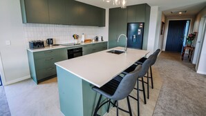 A modern kitchen with a central island, bar stools, and a refrigerator. - Fiordland Gateway by Aotearoa Escapes (Te Anau)