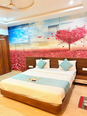 A hotel room with a large bed, a wooden headboard, and a wall mural depicting a tree and flowers. - Hotel Udaipur by Divine Inn (Udaipur)