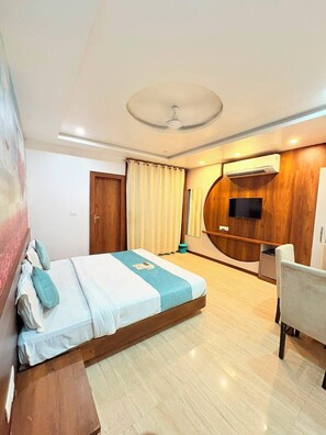 A modern hotel room with a bed, a desk, a chair, a TV, and an air conditioning unit. - Hotel Udaipur by Divine Inn (Udaipur)
