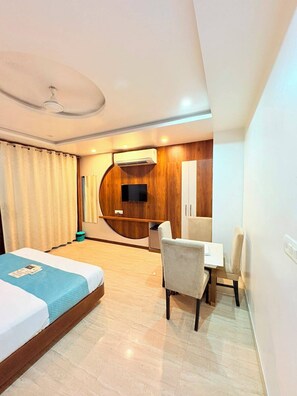 A hotel room with a bed, a desk, a chair, a television, and an air conditioning unit. - Hotel Udaipur by Divine Inn (Udaipur)
