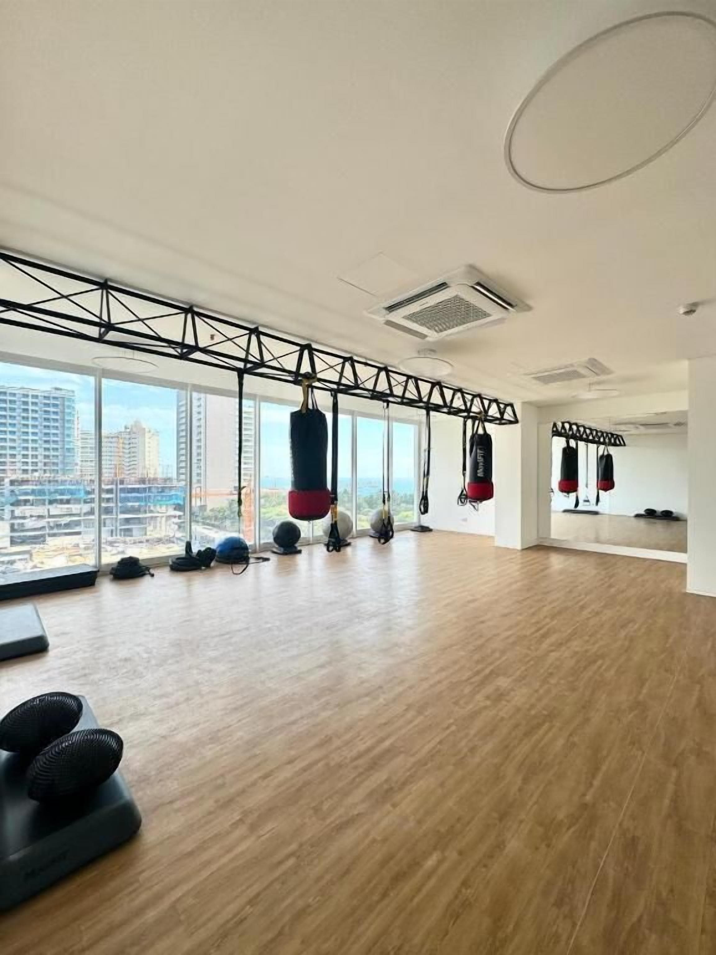 Une salle de sport spacieuse, dotée de grandes fenêtres, de ventilateurs de plafond et de divers appareils d’exercice.