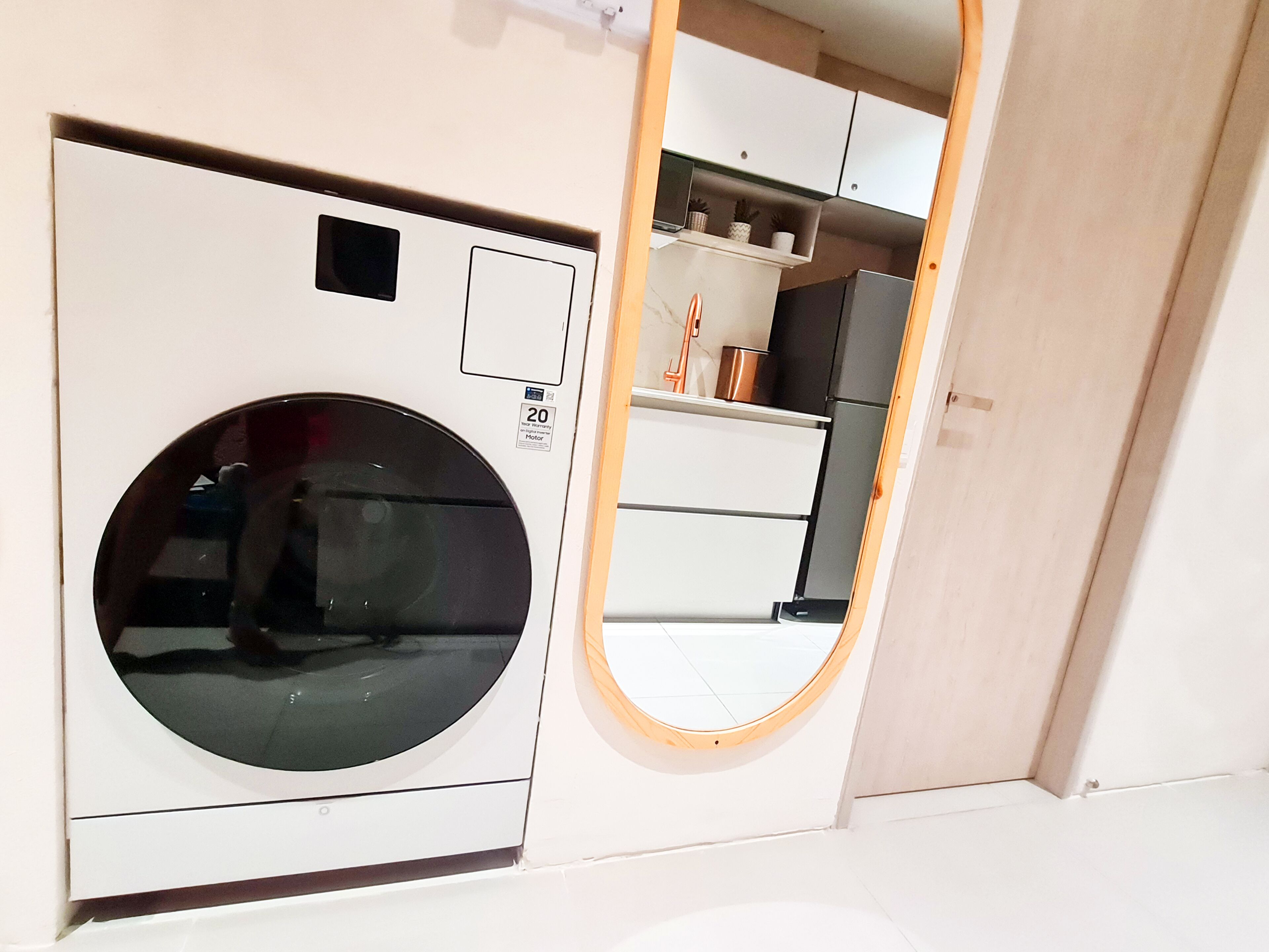 Quarto compacto com máquina de lavar, pequena cozinha e espelho.
