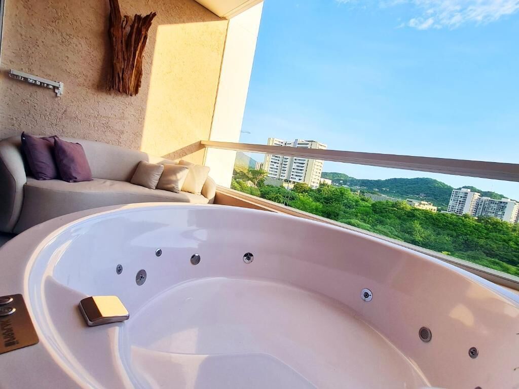 Un balcon doté d’un jacuzzi, d’un canapé et offrant une vue sur les bâtiments et la verdure.