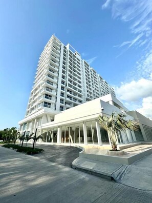 Un moderno hotel de gran altura con una entrada destacada, un área exterior cubierta y un cielo despejado.