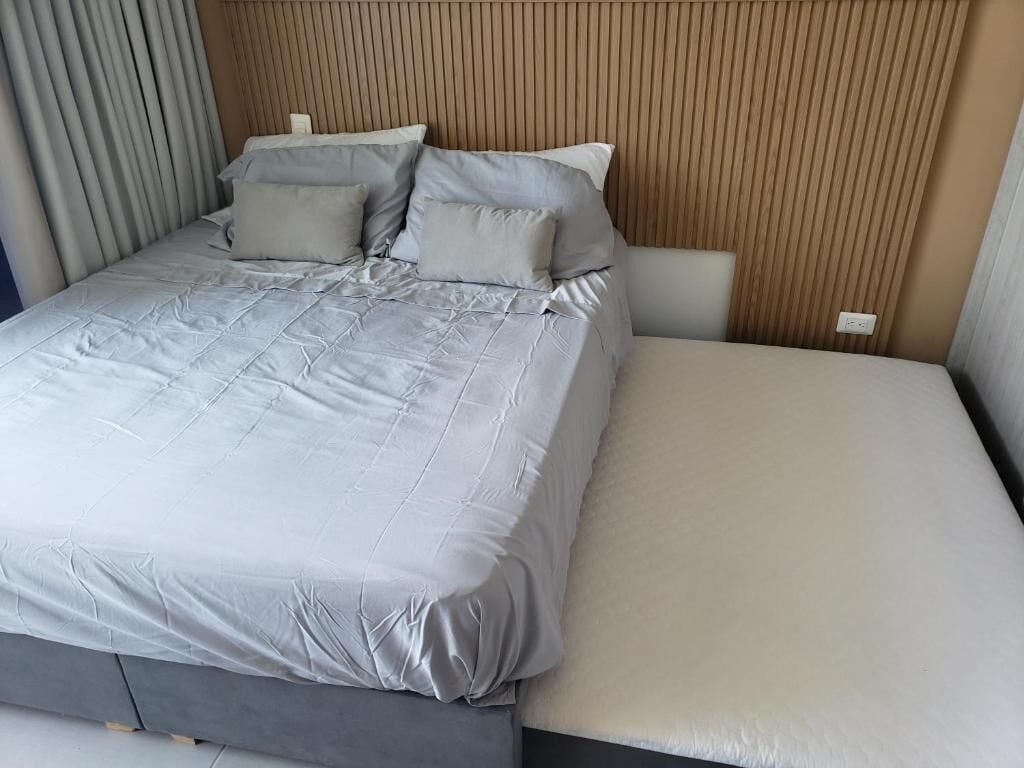Un lit avec une couette et des oreillers gris, une tête de lit en bois et une table de chevet.