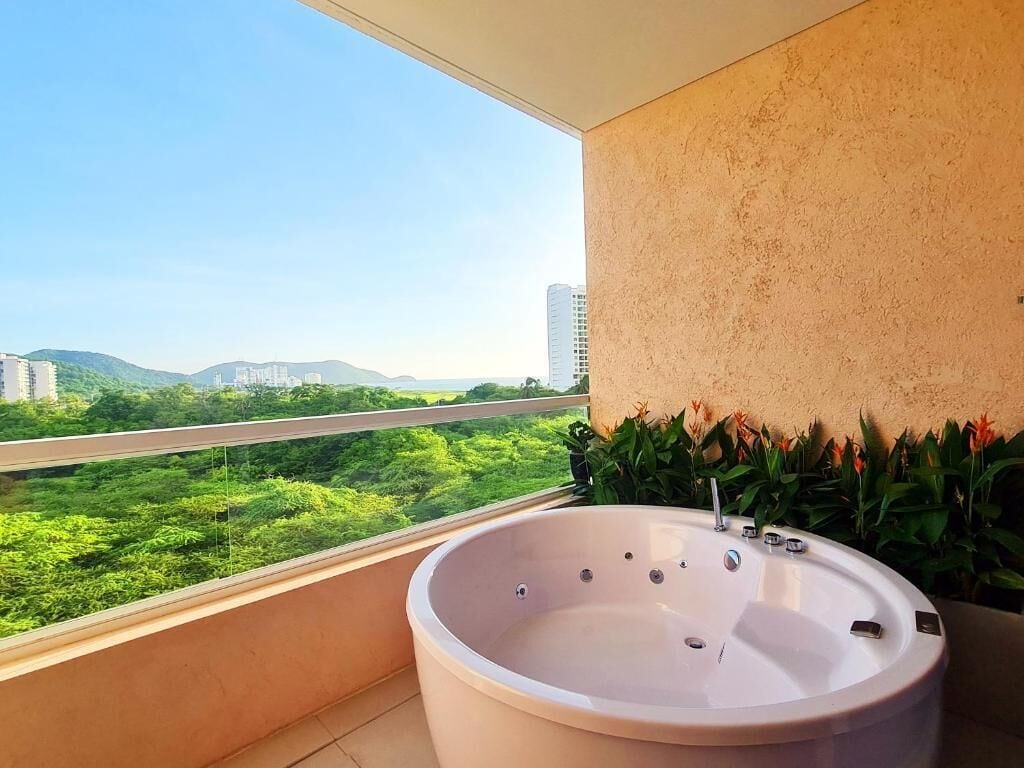 A balcony with a bathtub, a view of greenery and buildings, and a textured wall.