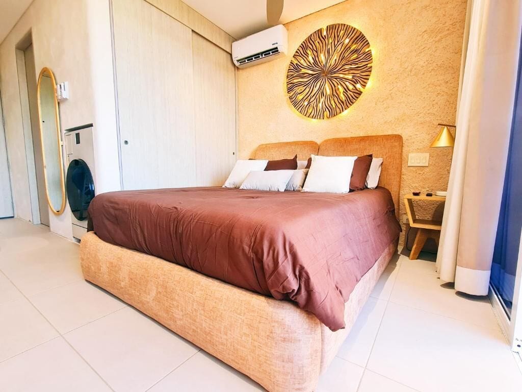 Quarto moderno com cama grande, decoração circular na parede, luminária de cabeceira e ar condicionado integrado.