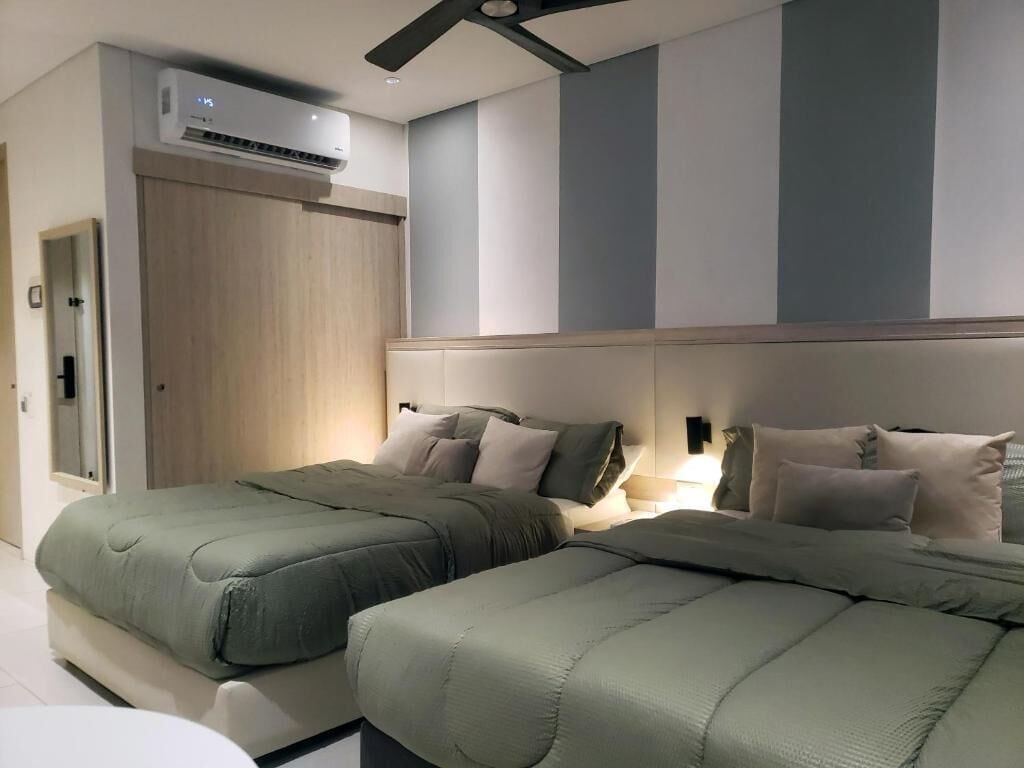 Una habitación de hotel moderna con dos camas, ventilador de techo, equipo de aire acondicionado y una paleta de colores neutros.