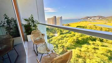 Un balcón con sillas de mimbre y una mesa, con vistas a un paisaje costero con edificios y vegetación.
