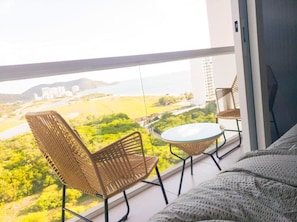Un balcon agrémenté de fauteuils en osier et d’une table en verre, offrant une vue sur un paysage verdoyant et des bâtiments.