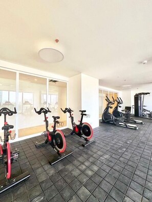 Une salle de sport équipée de vélos d’appartement et de tapis de course, dotée de grandes fenêtres et d’un éclairage au plafond.