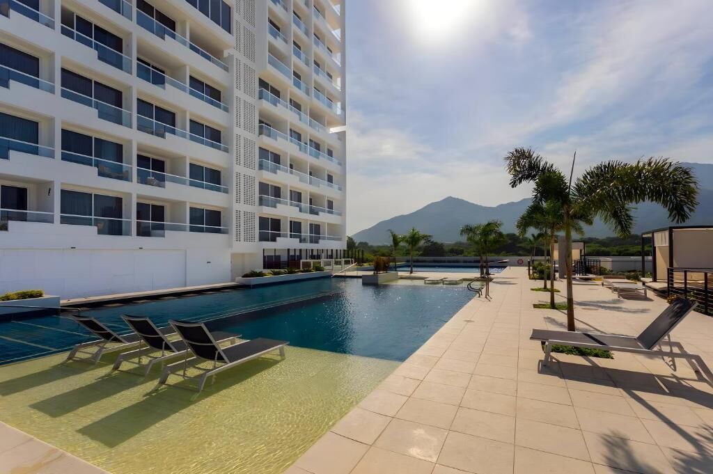 A modern hotel with a swimming pool, sun loungers, and a view of mountains.