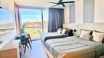 Una habitación de hotel moderna con una cama grande, un escritorio, una silla, un ventilador de techo y vistas a un paisaje montañoso.