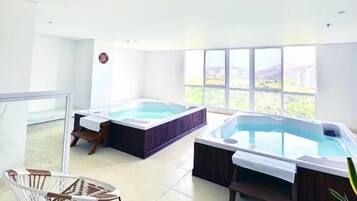 A spacious indoor area with two hot tubs, a glass partition, and a view of the outdoors.
