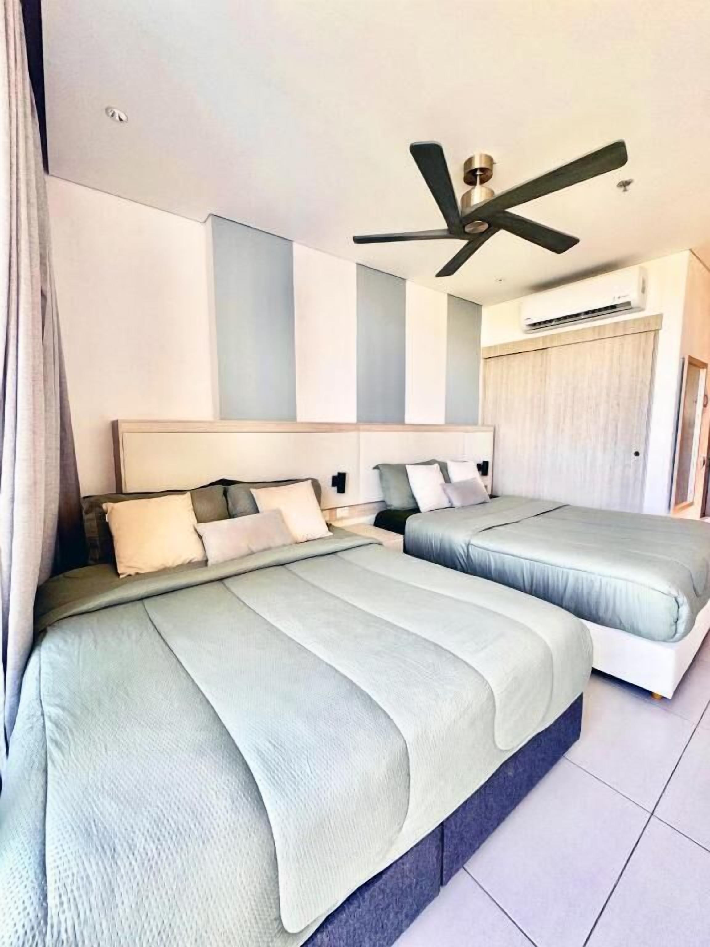 A hotel room with two beds, a ceiling fan, and an air conditioning unit.