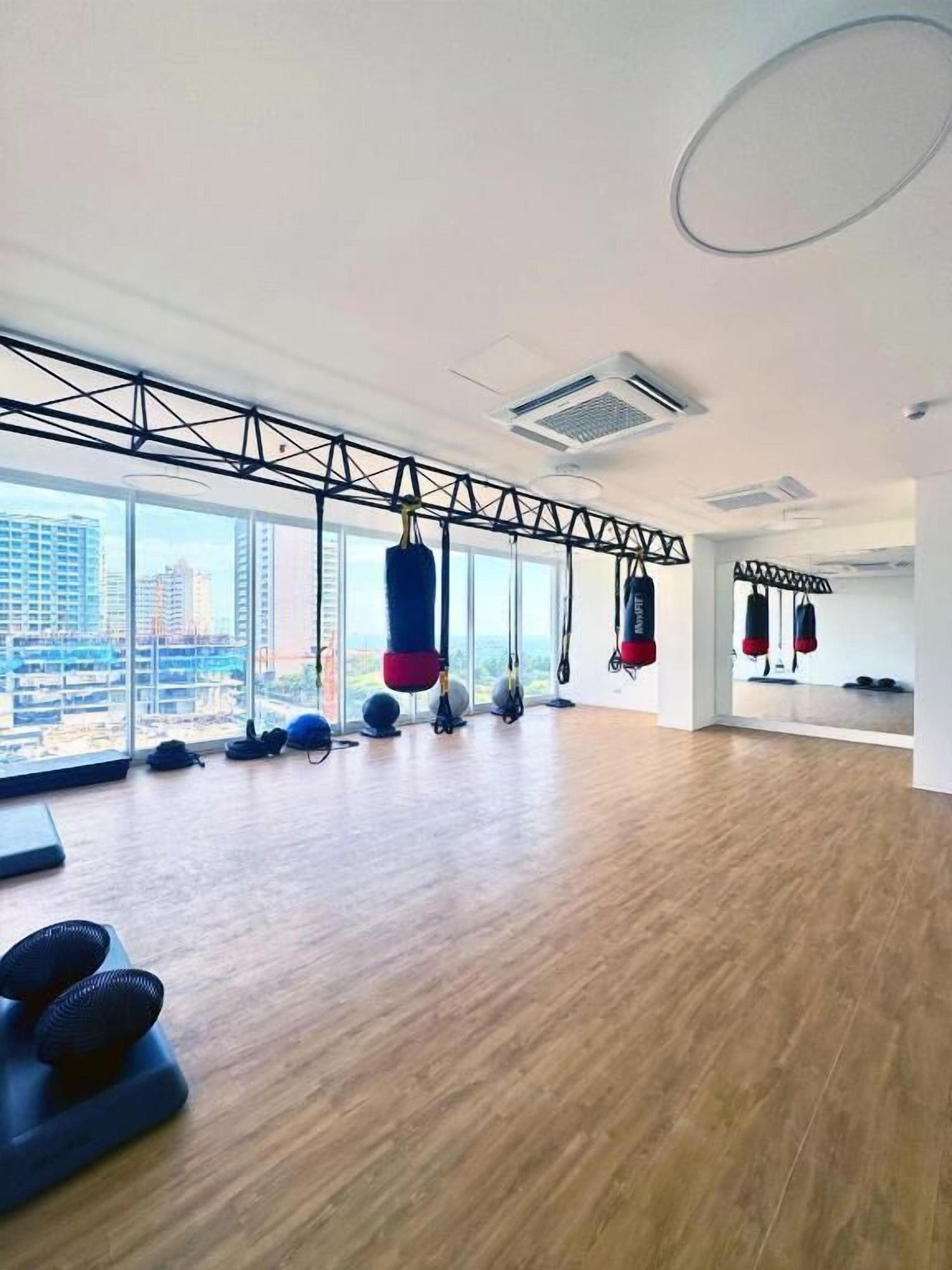 Un gimnasio amplio con ventanas grandes, sacos de boxeo y pelotas de ejercicio.