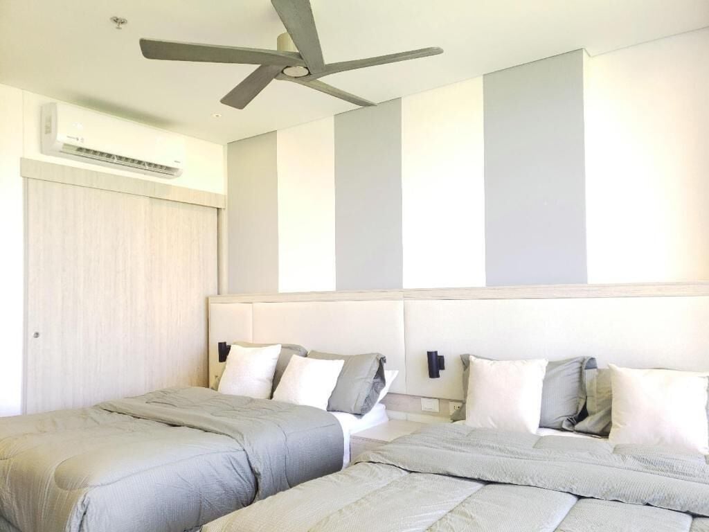 A hotel room with two beds, a ceiling fan, an air conditioning unit, and a light-colored wall with vertical stripes.