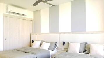 Habitación de hotel con dos camas, ventilador de techo, unidad de aire acondicionado y pared de color claro con rayas verticales.