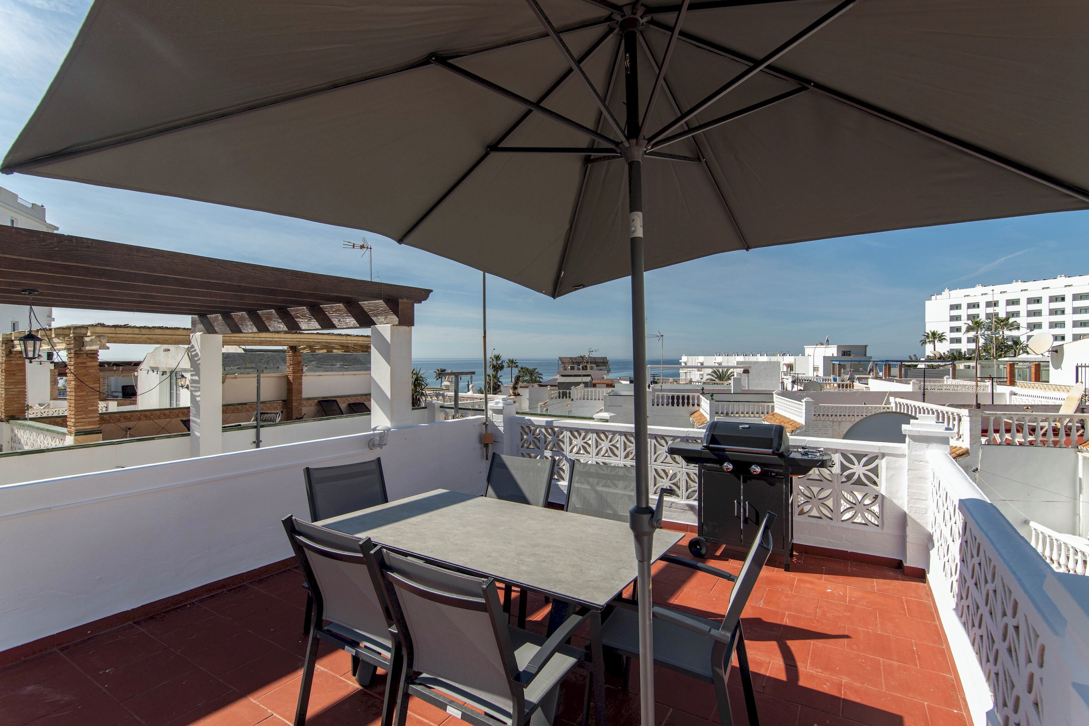 Terraza en la azotea con mesa y sillas, una parrilla y vistas de la ciudad.