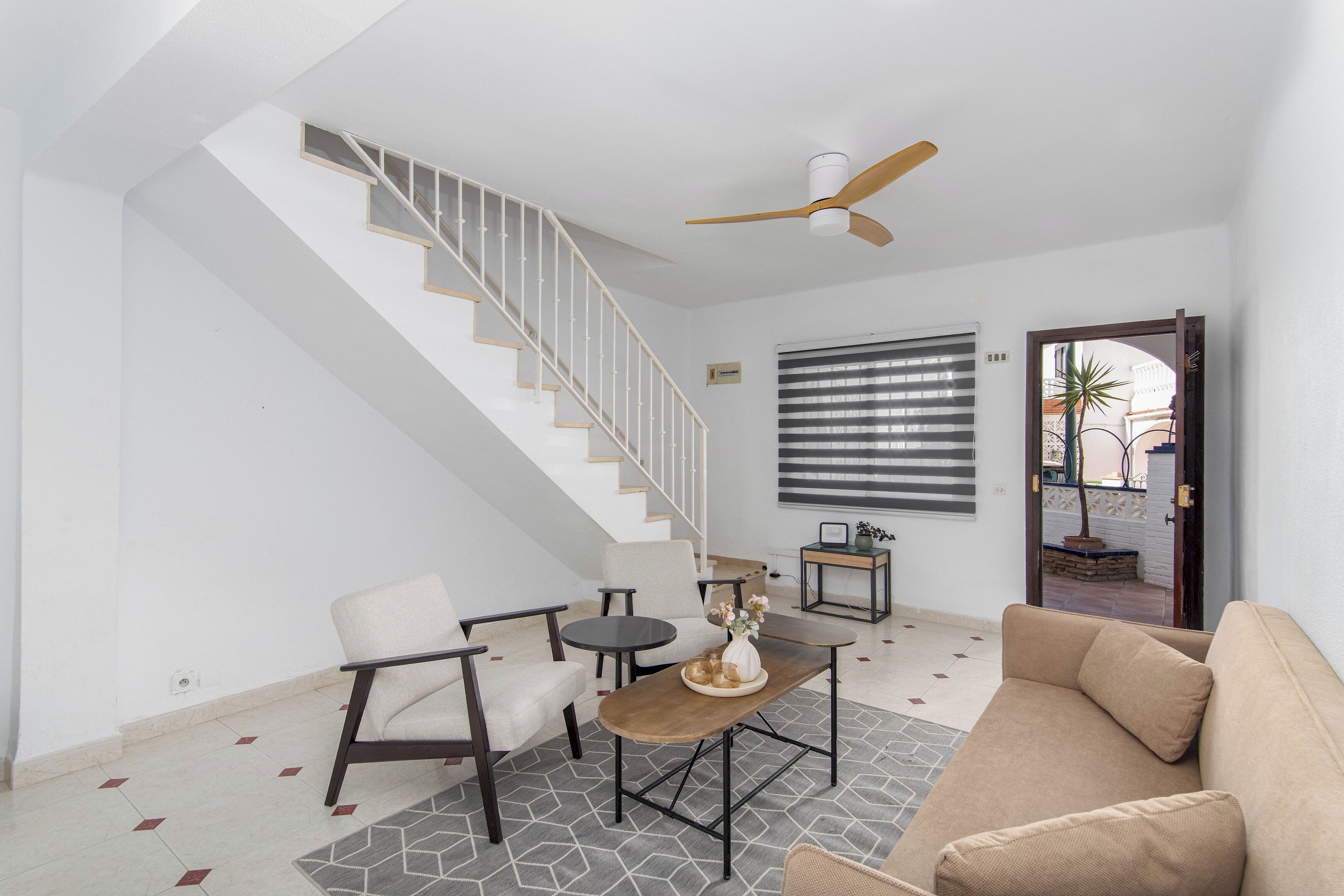 A modern living room with a staircase, a ceiling fan, a sofa, a coffee table, and a dining area.