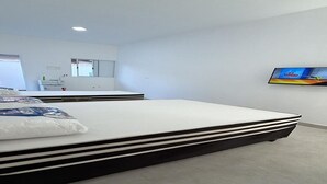 Una habitación de hotel moderna con una cama grande, un televisor en la pared y una pequeña zona de kitchenette.