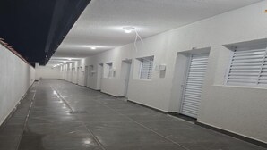 Un pasillo largo y estrecho con paredes blancas, suelo de baldosas y puertas con ventanas.