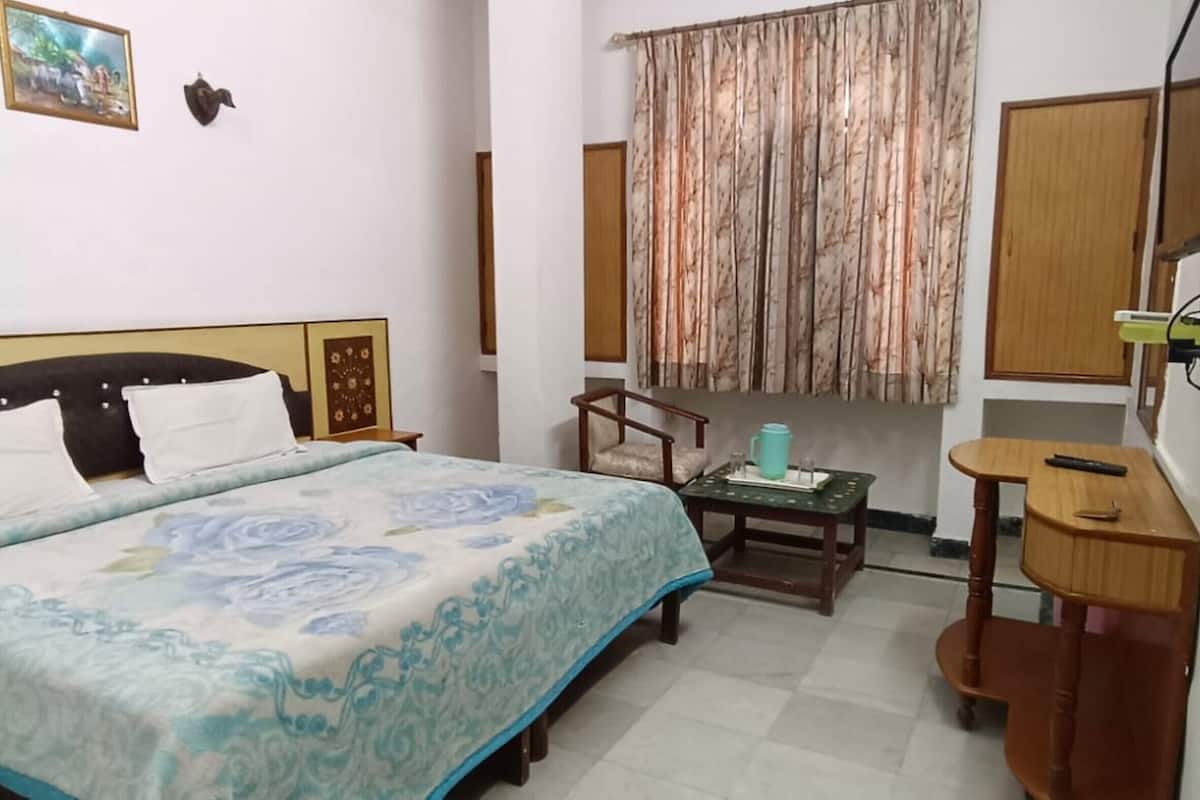 Une chambre à coucher avec un lit, une petite table, une chaise, un téléviseur et un rideau.