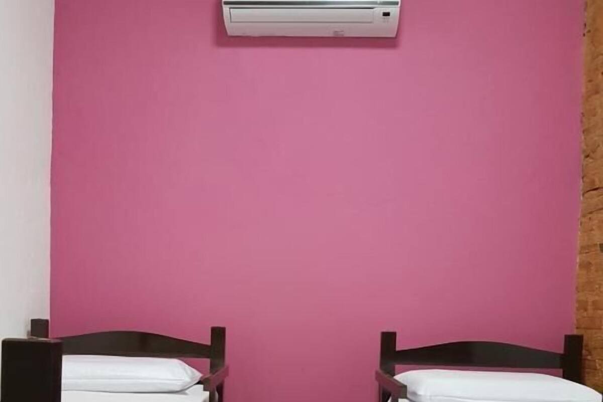 A room with two bunk beds, a pink wall, and an air conditioning unit.