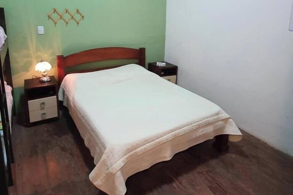 A single bed with a wooden headboard, a bedside table with a lamp, and a nightstand with a small drawer.