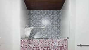 A bathroom with a shower, tiled walls, and a patterned shower curtain. - Hostel Casa de Avany (Cachoeira)