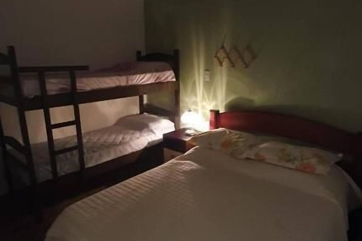 A room with bunk beds, a single bed, a nightstand, and a wall-mounted lamp.