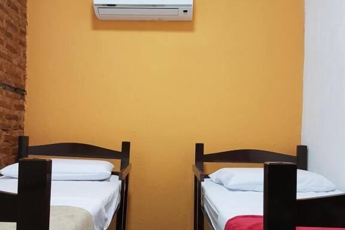 Two bunk beds with white and red bedding, a brick wall, and an air conditioning unit on the wall.
