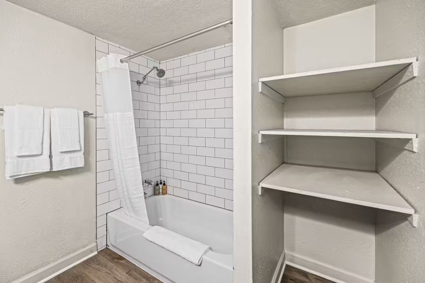 A bathroom with a shower, a bathtub, and white tiled walls. There are two white towels hanging on the wall and a shower curtain.