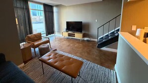 Ein modernes Wohnzimmer mit Flachbildfernseher, Ledersofa, Hocker und einer Treppe.
