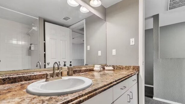 A bathroom with a sink, mirror, and granite countertop. - Superbly Located 2 BR Loft Apartment Downtown ATX (Austin)