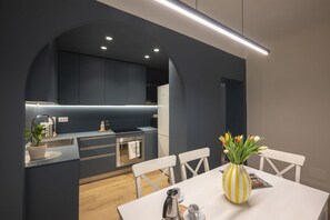 A modern kitchen with dark cabinetry, a white dining table, and a vase with flowers. - Apartments Florence - San Marco Design Apartment (Firenze)