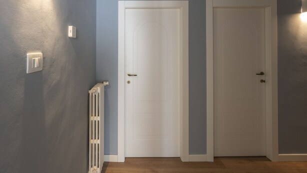 Un couloir avec deux portes blanches, un radiateur et un interrupteur sur le mur.