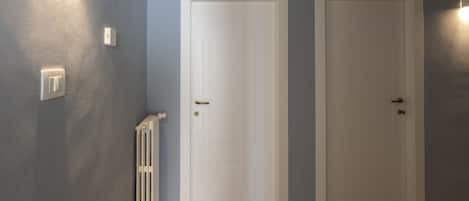 A hallway with two white doors, a radiator, and a light switch on the wall.