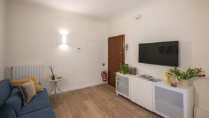 Un salon avec un canapé, un tél éviseur, une console blanche et une porte.