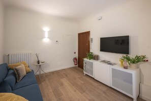 Ein Wohnzimmer mit einer Couch, einem Fernseher, einer weißen Konsole und einer Tür.