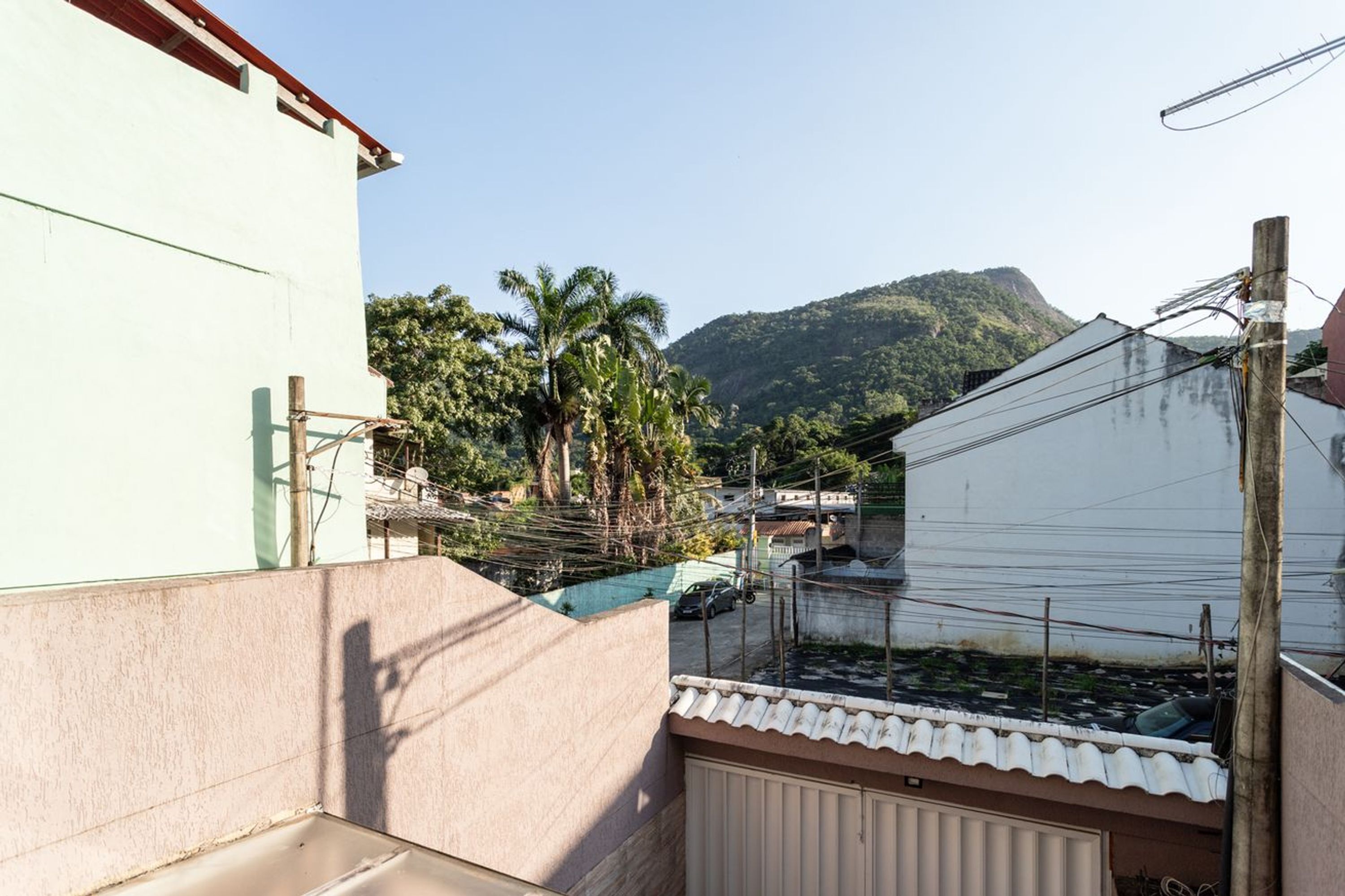 A residential area with a white building, a fenced yard, and a mountain in the background.