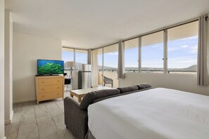 Quarto de hotel com cama, escrivaninha, poltrona, televisão e vista para a cidade.
