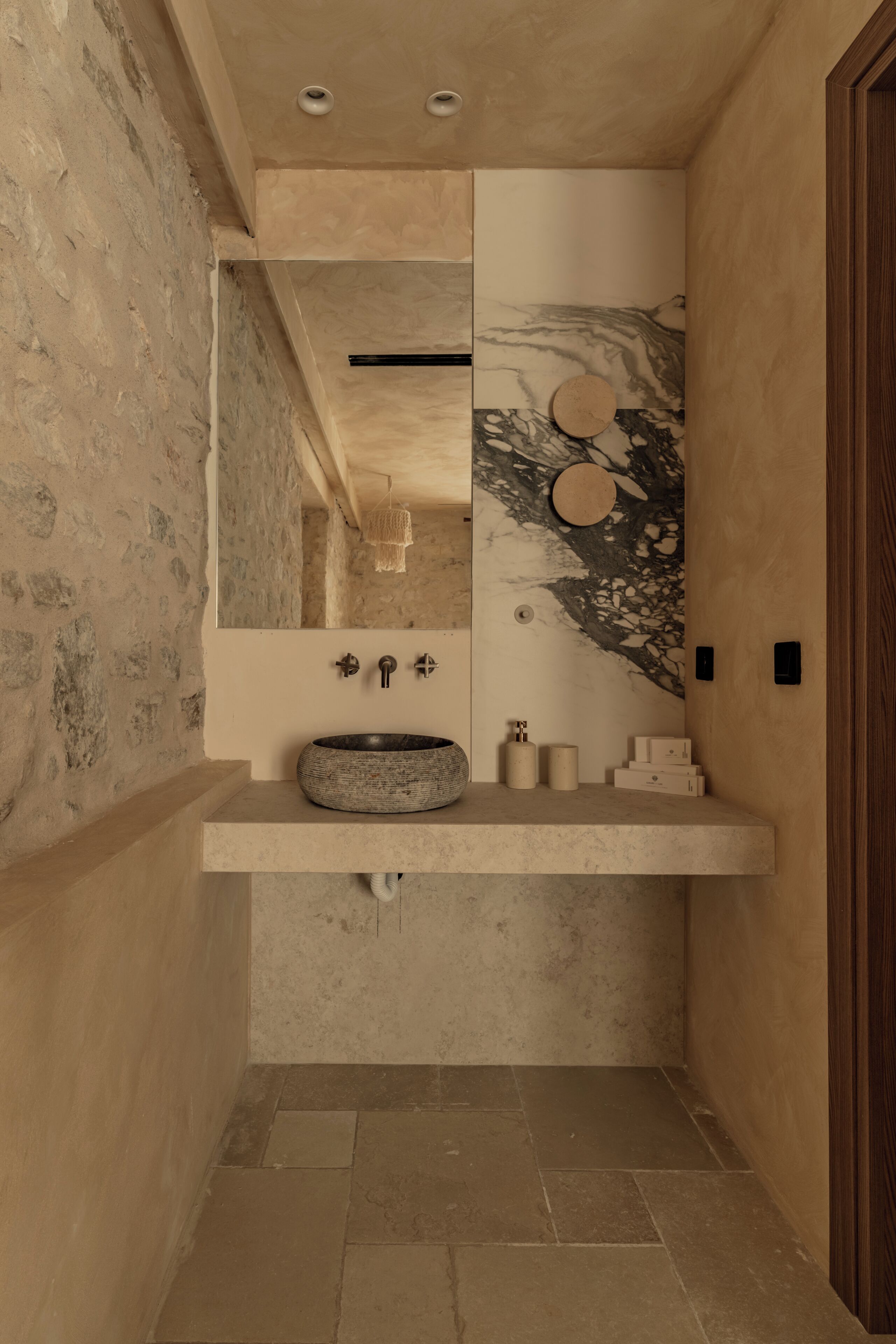 Un baño con un lavamanos de piedra, un espejo y una puerta de madera.