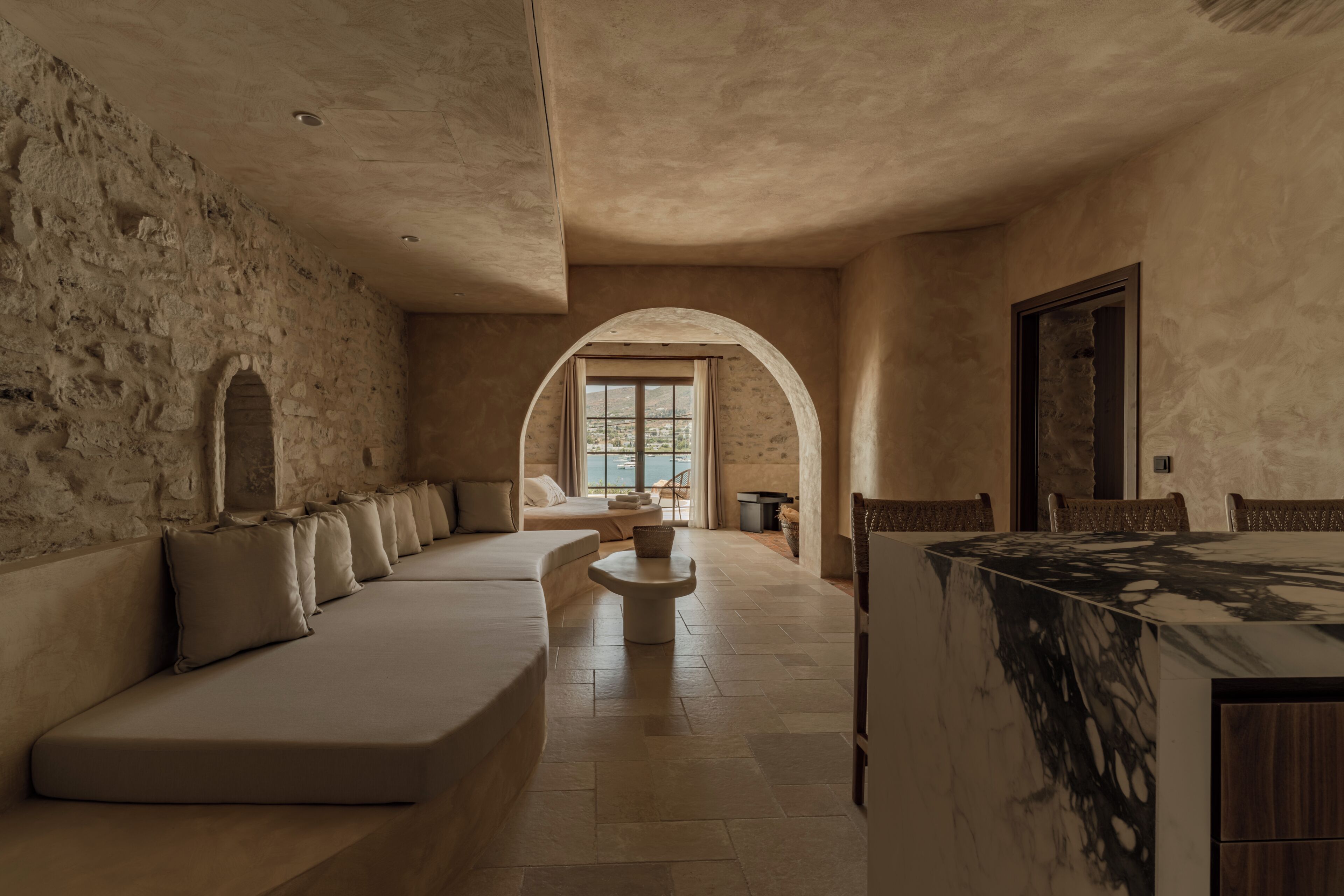 A spacious room with a long sofa, a dining table, and a view through an arched window.