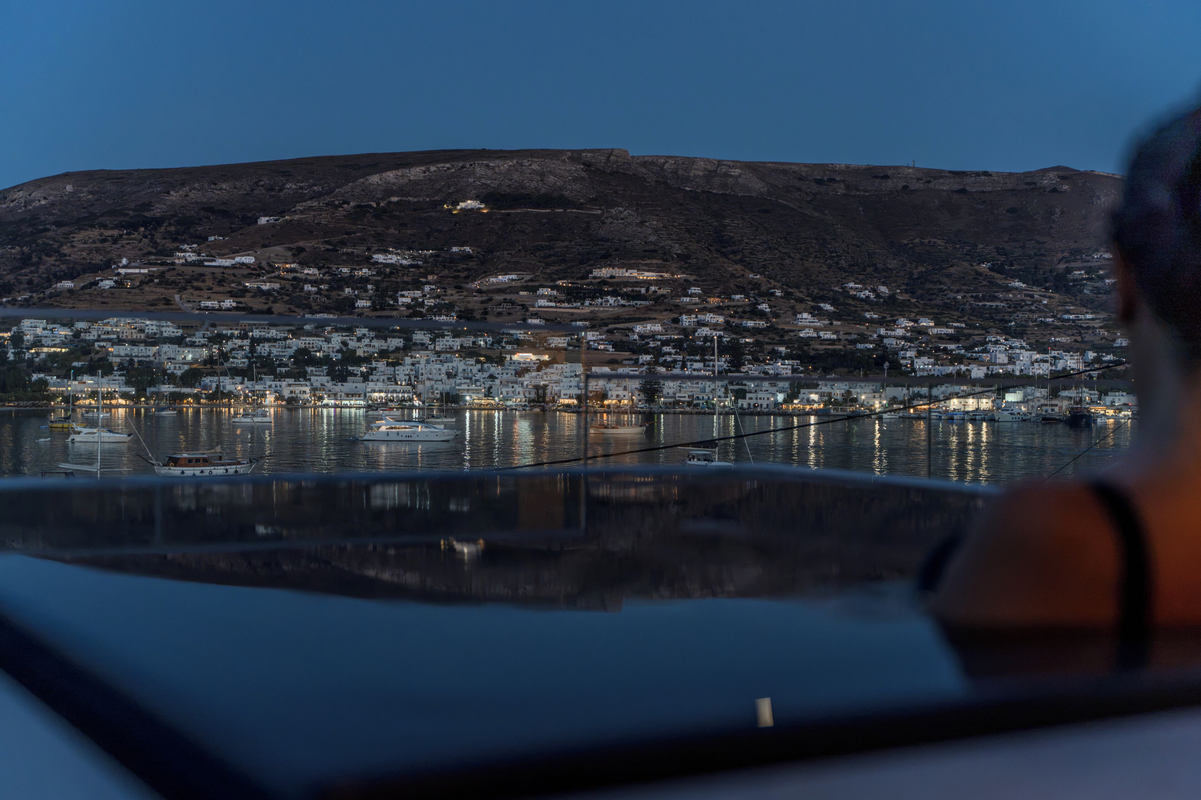 A coastal town with buildings along the waterfront, a body of water in the foreground, and a hill in the background.
