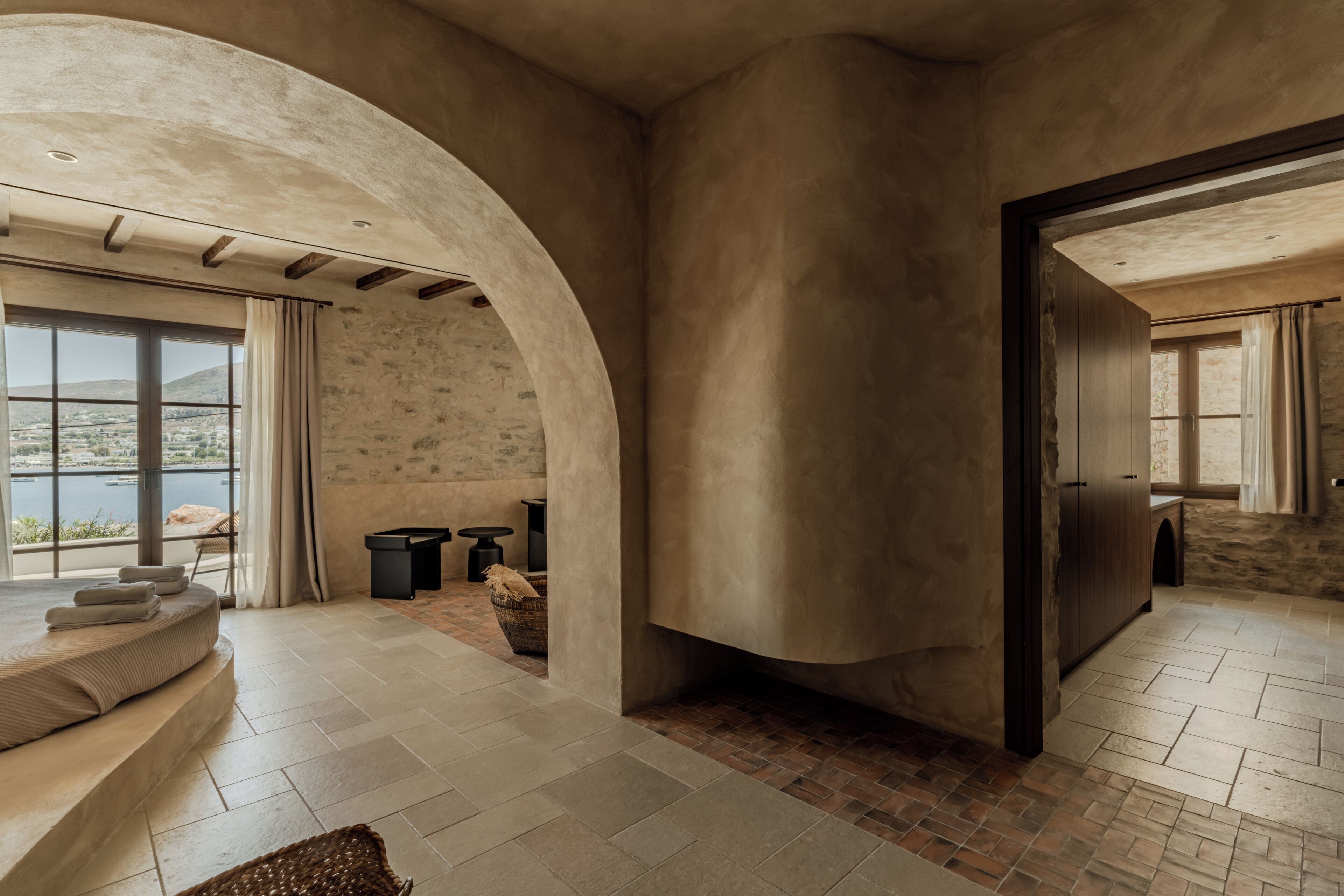 Una habitación amplia con un gran arco de entrada, una zona de estar con un banco y cojines, y vistas al exterior a través de un ventanal.