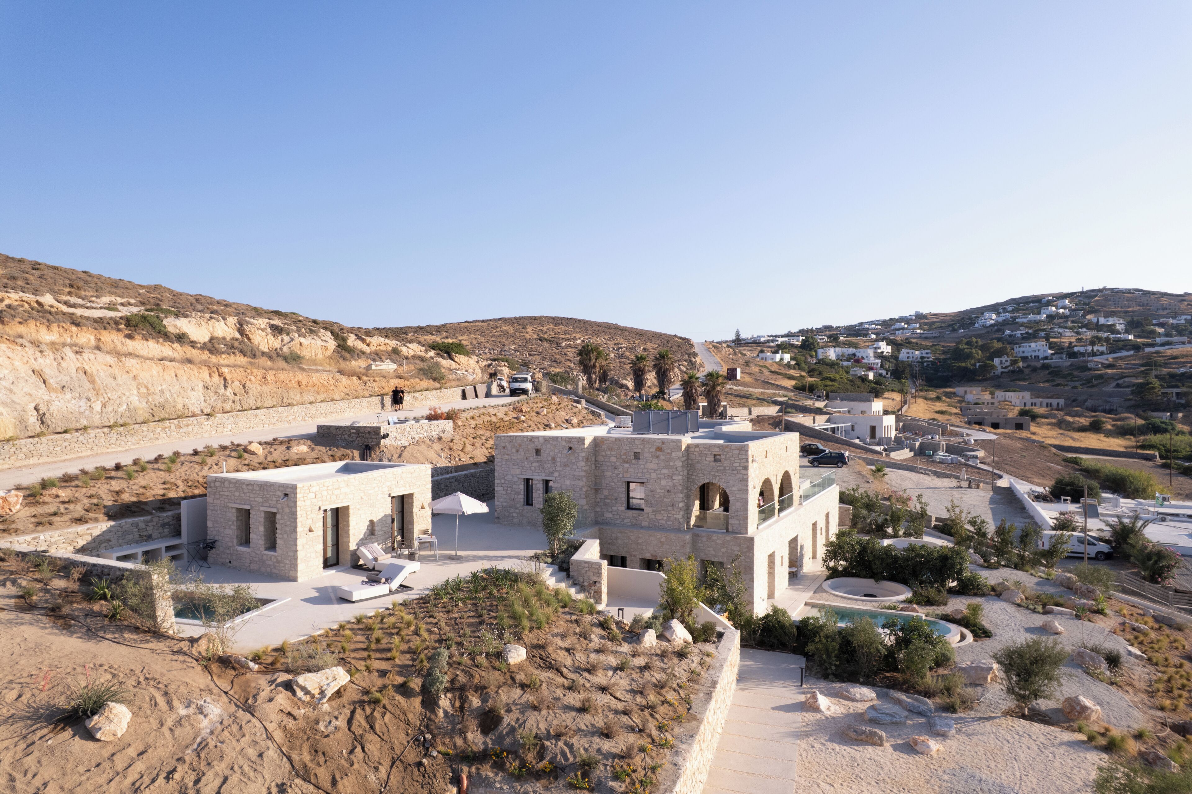 A modern building with a pool, surrounded by a rocky landscape and a distant village.