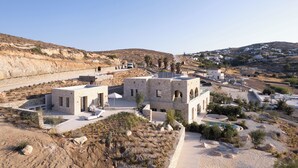A modern building with a pool, surrounded by a rocky landscape and a distant village. - Eunoia Suites (Paros)