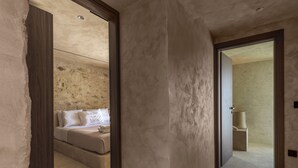 A hallway leading to a bedroom with a bed and a bathroom. - Eunoia Suites (Paros)